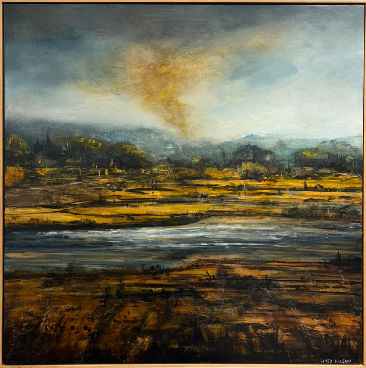 Mixed media painting of a river landscape by Lyndy Wilson, with golden riverbanks, reflective water and distant hills beneath a dramatic grey sky illuminated by warm evening light